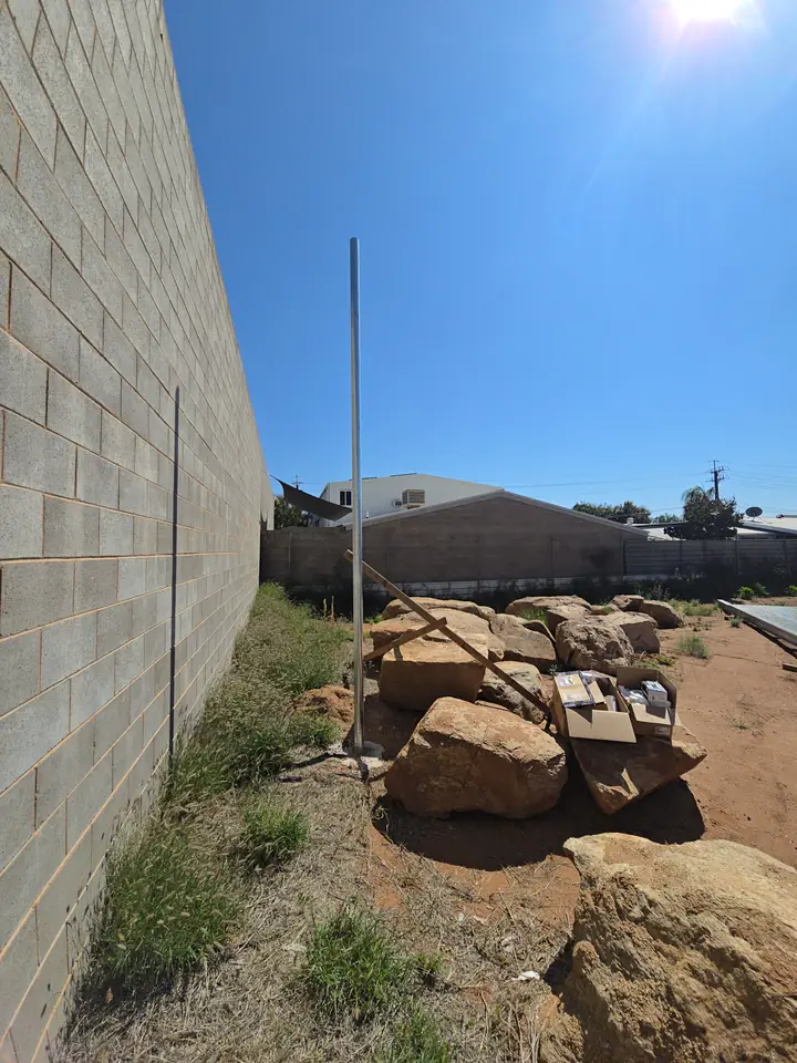 A bare galvanised pole standing against a block wall, before anything is fitted