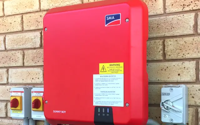 An SMA Sunny Boy solar inverter with DC isolators and an AC isolator on a brick wall, installed by Sawtell Contracting NT