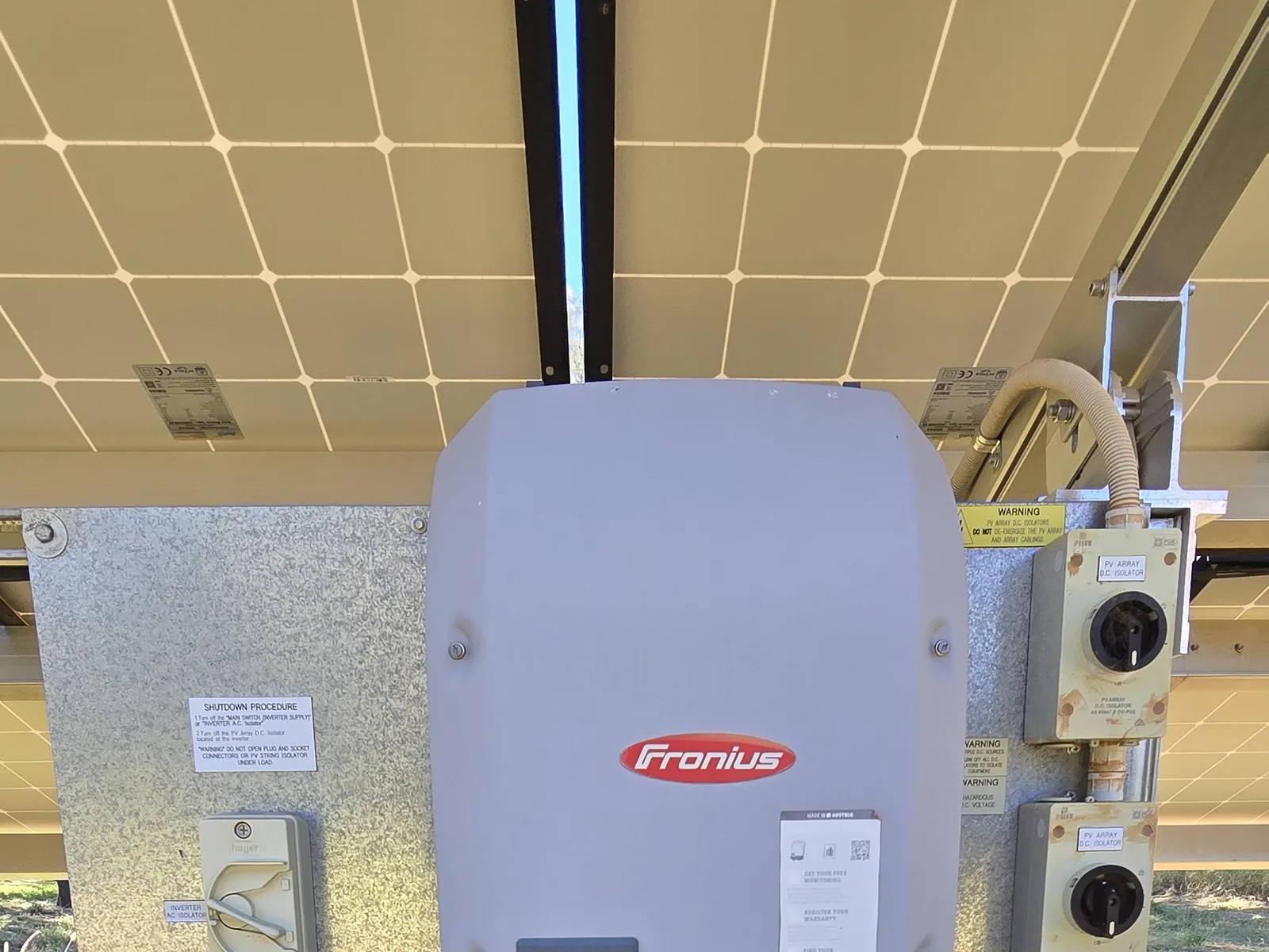 Fronius Symo grid-connect solar inverter with dual PV array DC isolators, mounted beneath a ground-mount panel array. A real Sawtell Contracting NT solar installation near Alice Springs