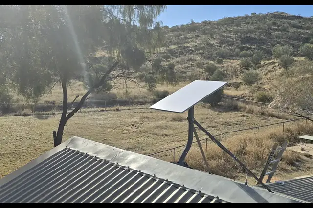 Satellite dish mounted on a corrugated iron roof, with dry hills behind, on a rural job in Central Australia