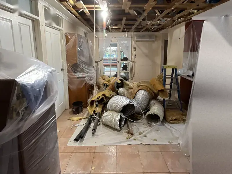 Old cooler ductwork pulled out and lying on the floor of a room with the ceiling open and furniture covered in plastic