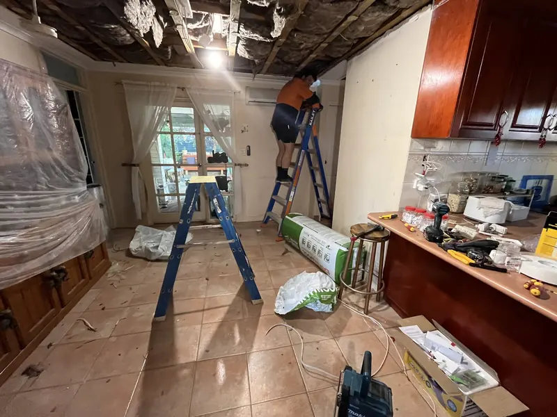 Jacob Sawtell on a ladder working in the open ceiling, with new insulation batts ready to go in